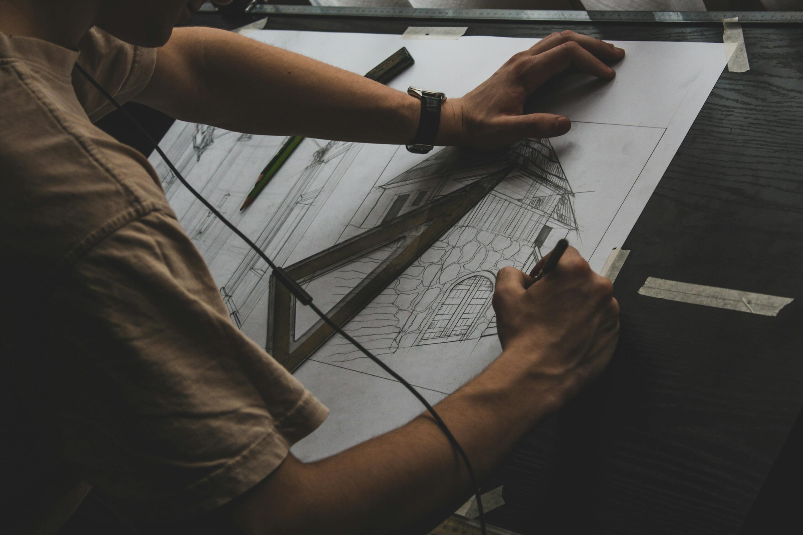 A person sketching architectural designs using traditional tools on a desk.