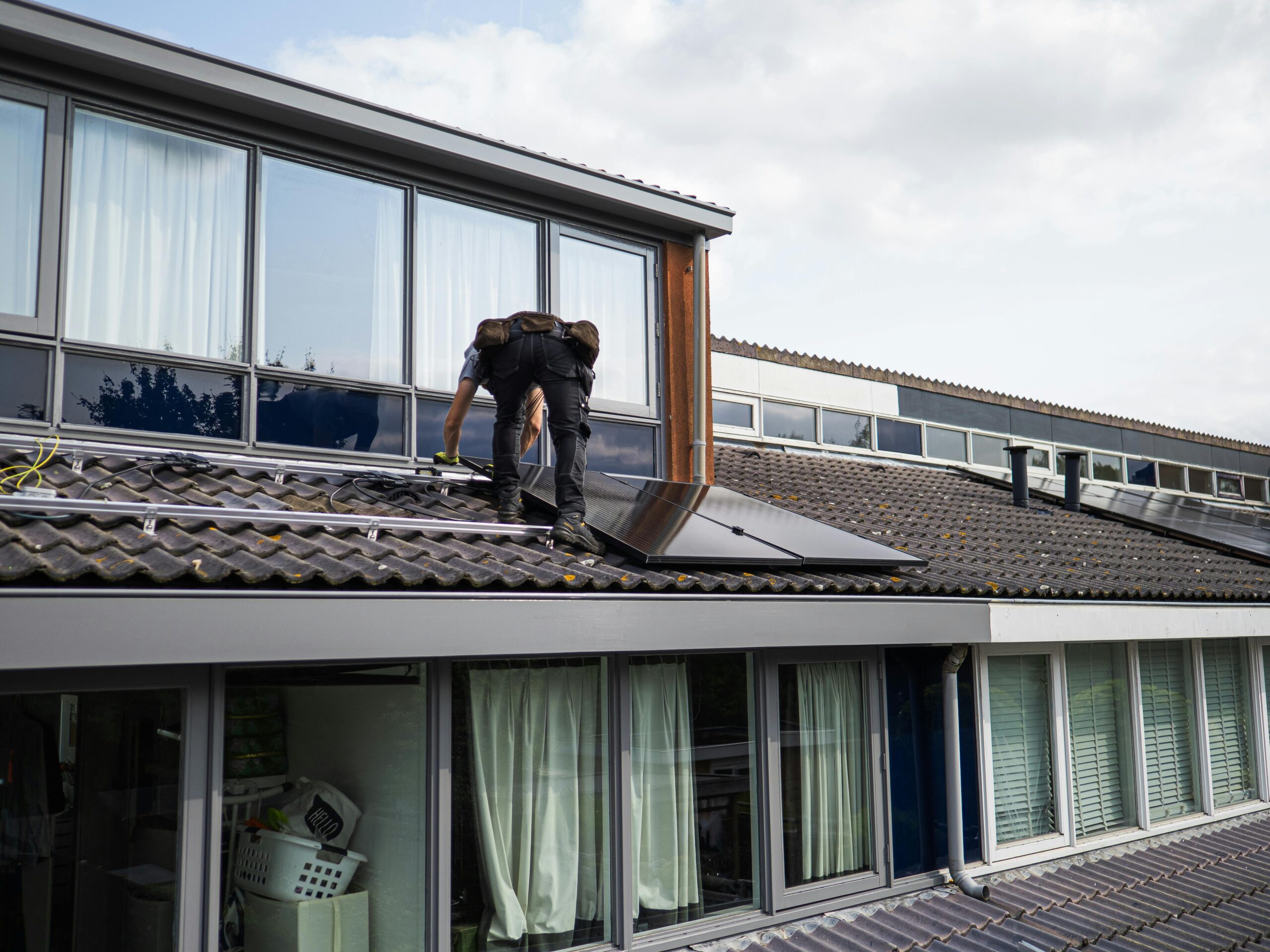 Technician working on installing solar panels on a residential rooftop during the day.