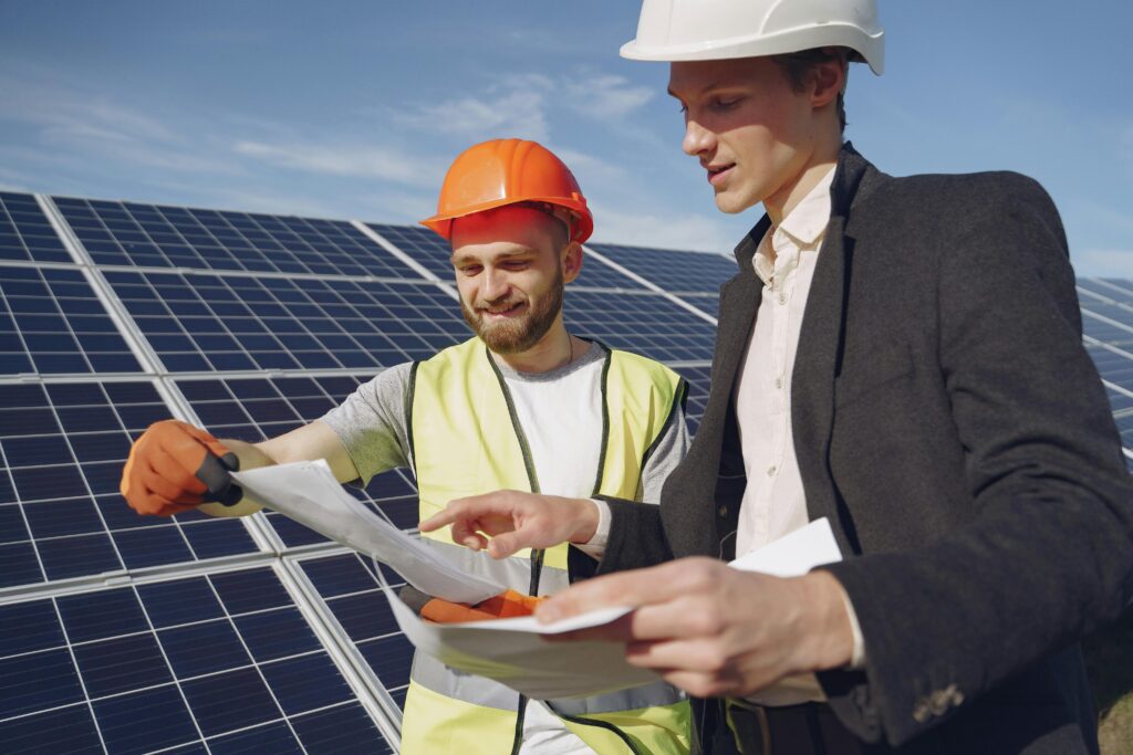 Two engineers reviewing plans for solar panel installation, representing teamwork in renewable energy.