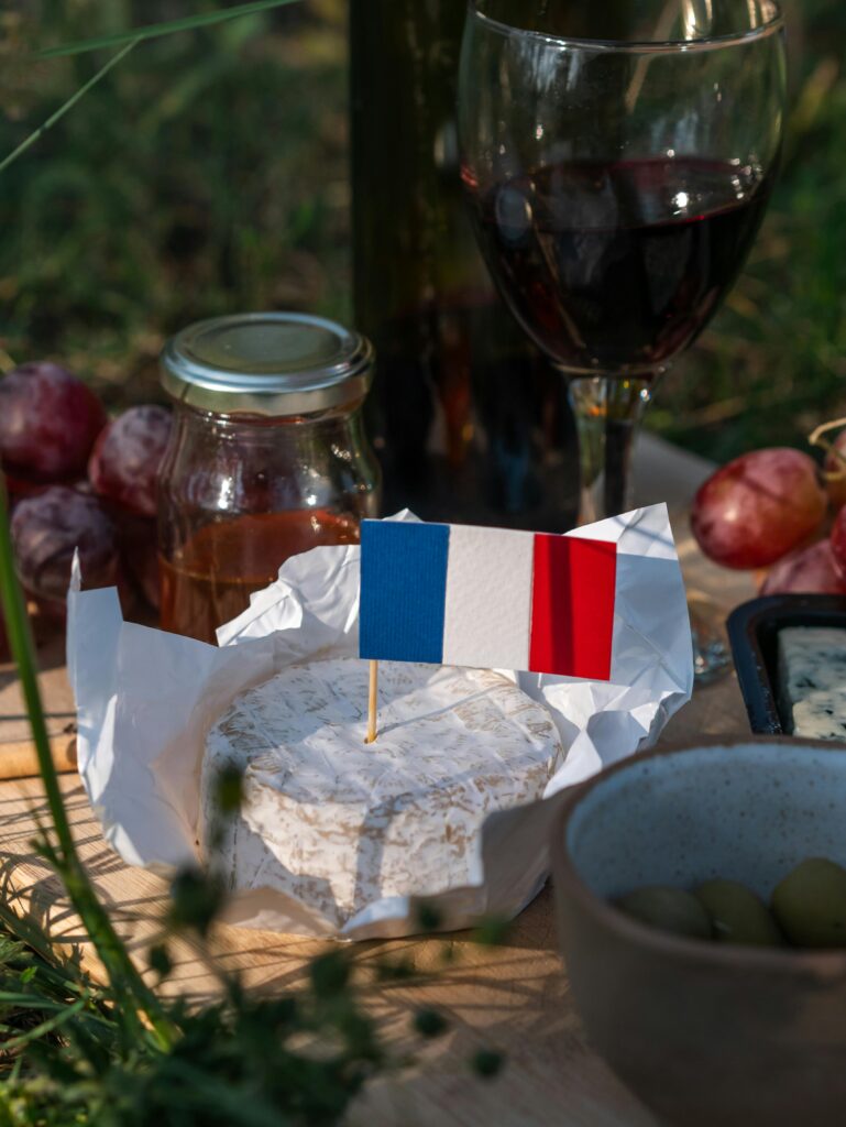 A rustic French picnic featuring camembert cheese, red wine, and a French flag for a celebratory feel.