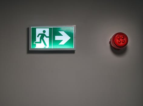A brightly lit exit sign and alarm in an indoor corridor, indicating emergency escape route.