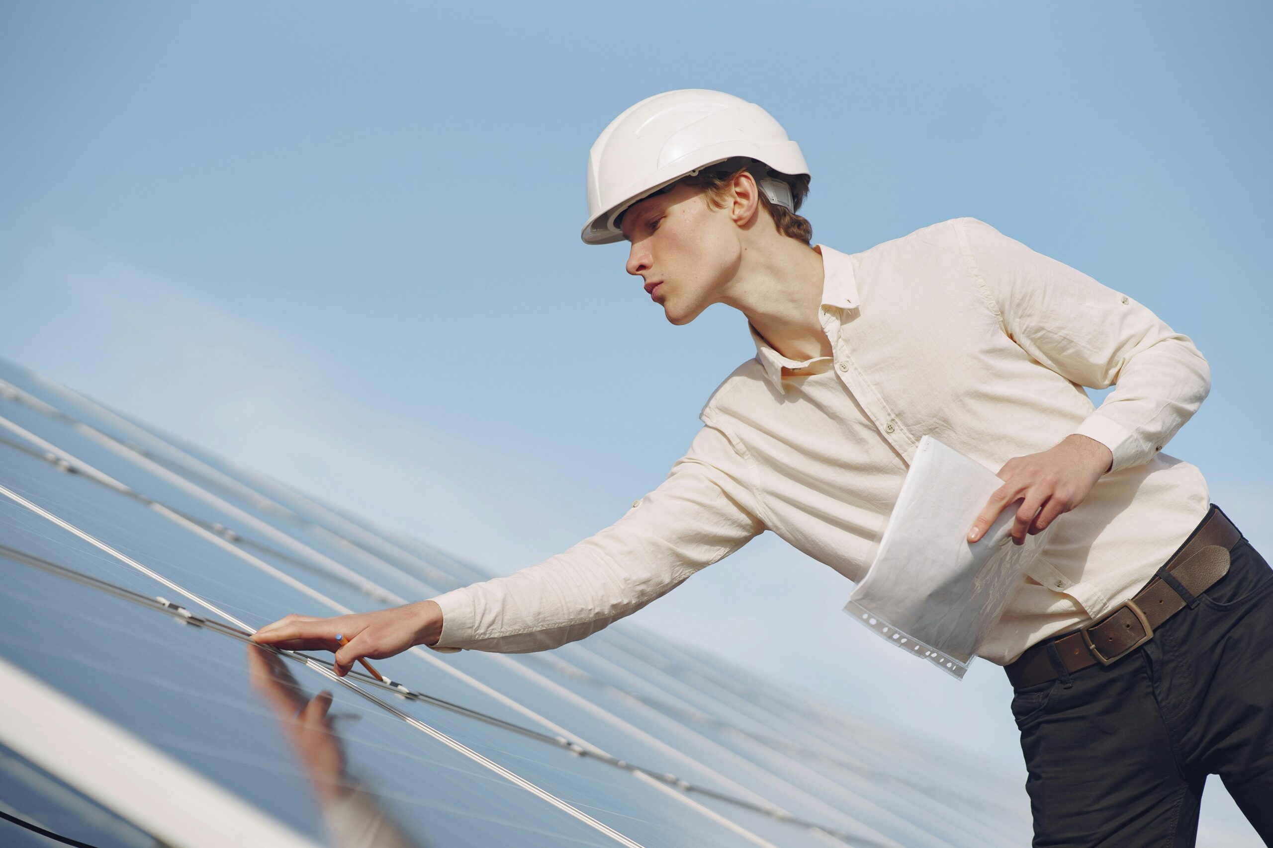 A solar technician in a hard hat inspecting photovoltaic panels under clear skies.