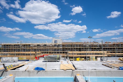 Wide-angle shot of a construction site with scaffolding and materials under a clear blue sky.