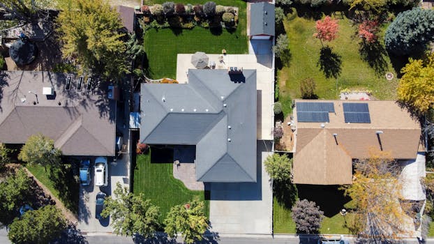 Drone shot capturing rooftops, solar panels, and green lawns in South Jordan, Utah.