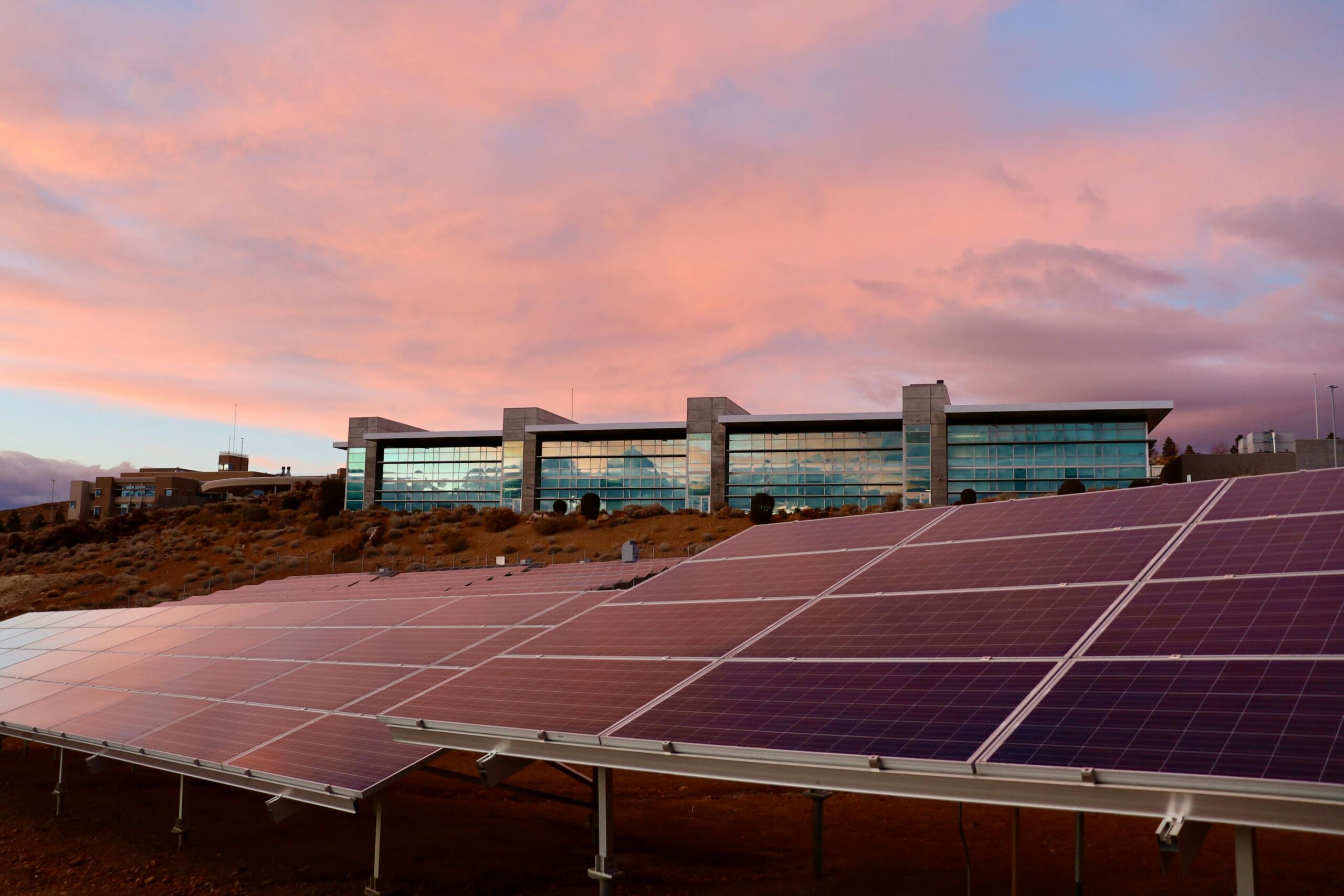 Solar panels in front of a modern building at sunset showcasing renewable energy technology.