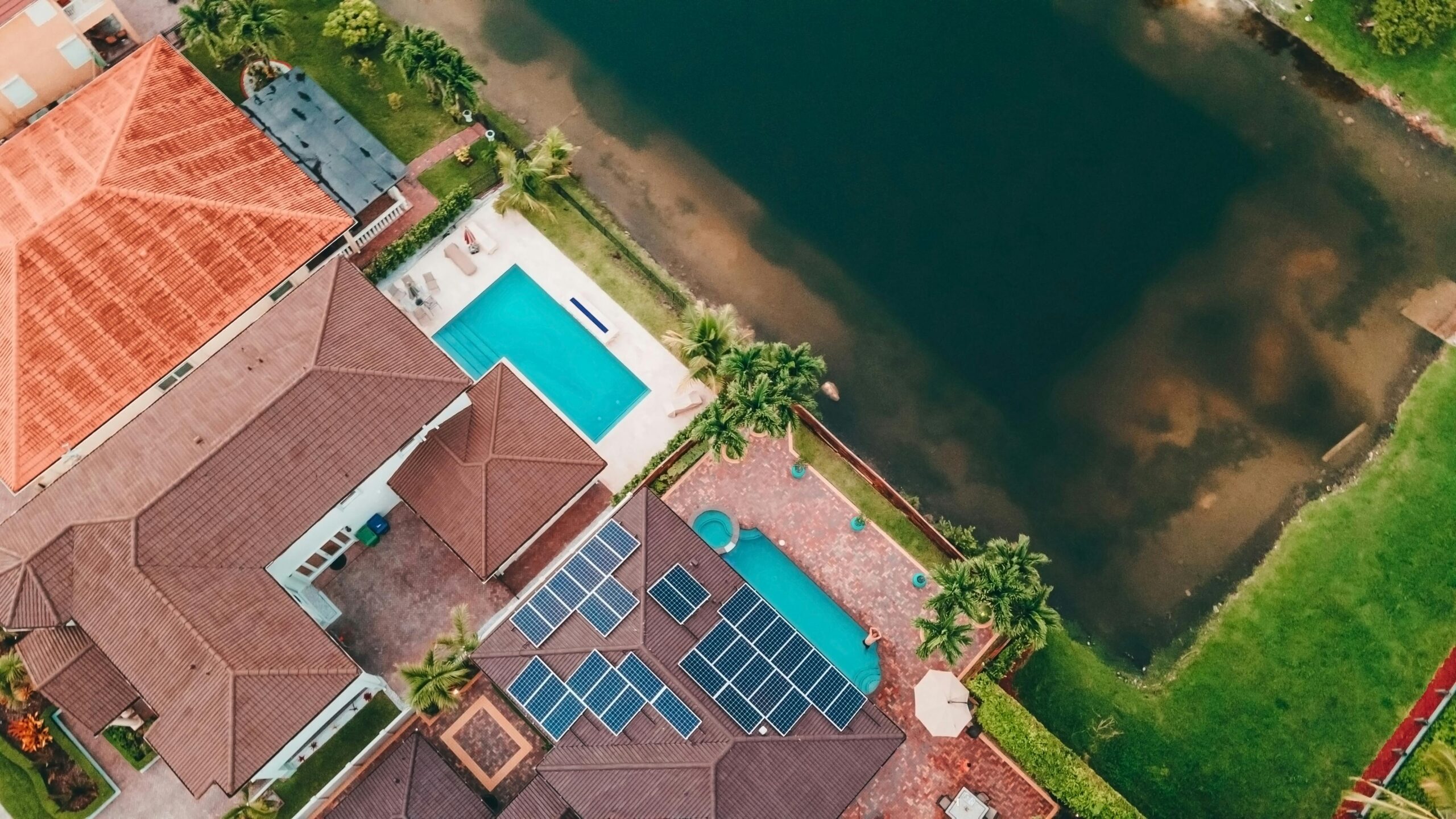 Top-down view of a Miami home with solar panels and pool near a lake.