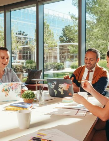 Three colleagues brainstorming with laptops in a well-lit office.